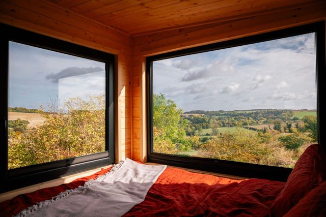 Corner windows framing a wooded valley from the bed of an off-grid cabin